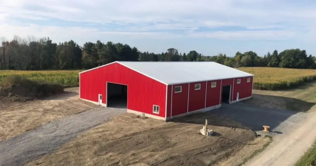 Large red agricultural steel building in Ontario with white roof surrounded by farmland and open fields