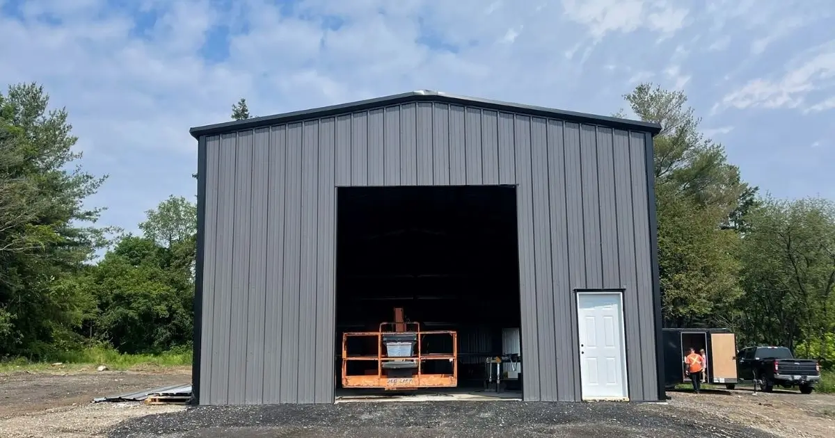Large custom steel building in Ontario with wide front opening and white side door under blue sky built by Tower Steel Buildings