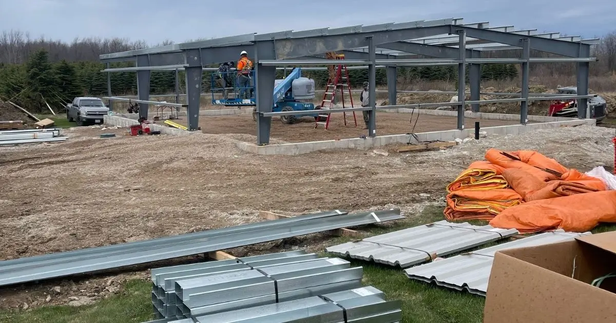 Steel building frame under construction in Ontario with beams, ladders, and workers installing structure on concrete foundation