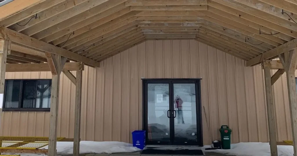 Post-frame steel building in Ontario with wooden truss entry and beige metal panels during winter