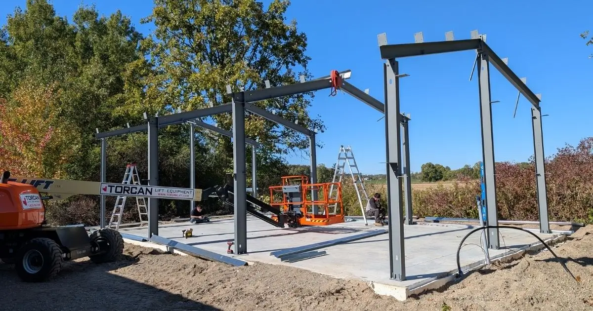 Crew assembling a steel building frame on a concrete foundation under clear blue Ontario sky