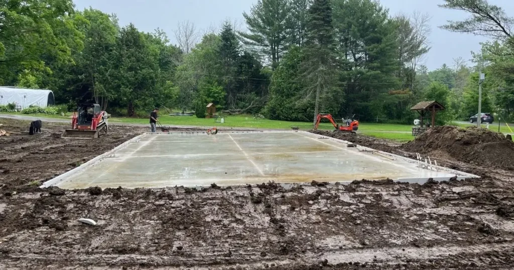 Contractors leveling a freshly poured steel building foundation on a muddy Ontario job site
