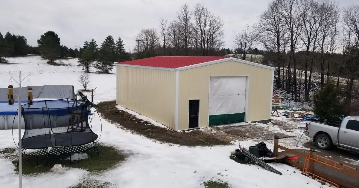 Beige steel building with red roof in snowy Ontario backyard beside pickup truck showing durability over wood construction