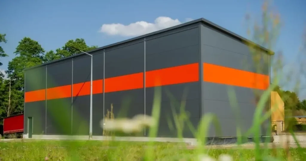Modern steel warehouse building in Ontario with grey and orange panels surrounded by greenery under blue sky
