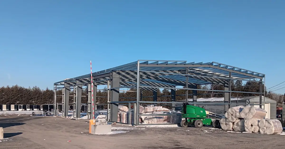 Steel building frame under construction for an auto repair shop in Canada with clear span bays, vehicle access openings, and roof framing installed.