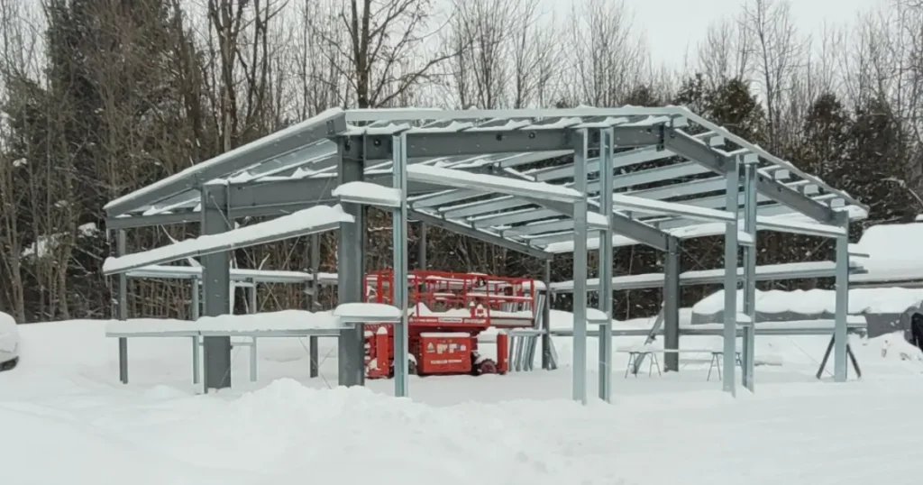 Steel building frame under construction in winter conditions, showing structural design elements that influence pricing changes in Canada