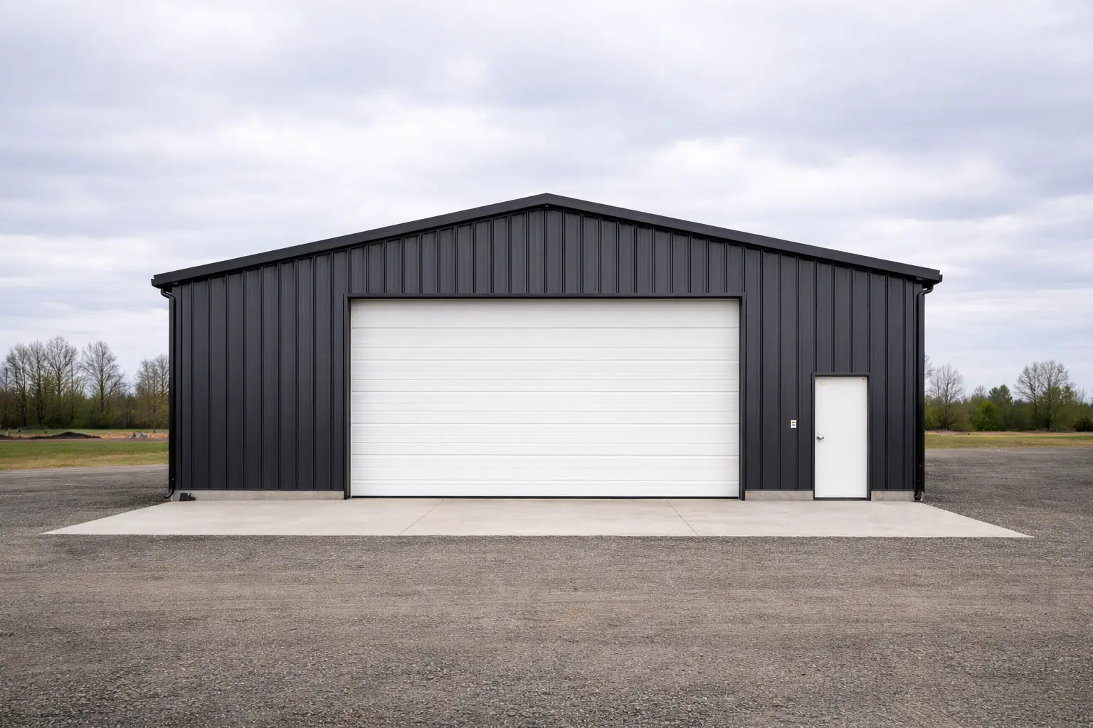 Front 3/4 view of 30x50x16 clear-span steel shop building with charcoal metal siding and overhead door on concrete slab.