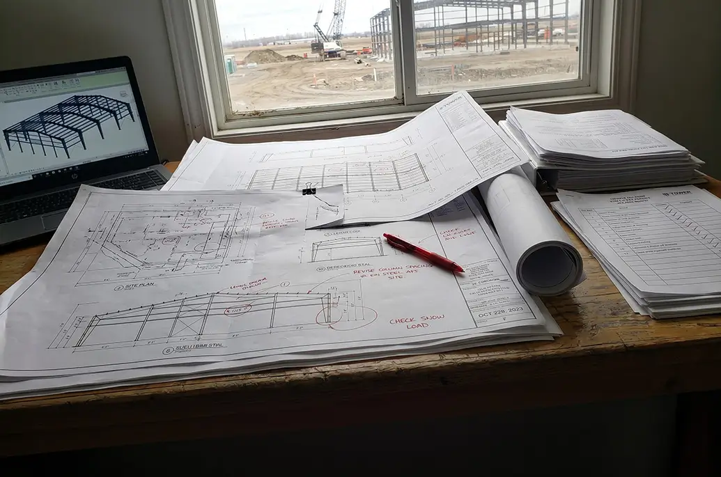 Steel building permit timeline Alberta with drawings and active construction site showing permit stage coordination